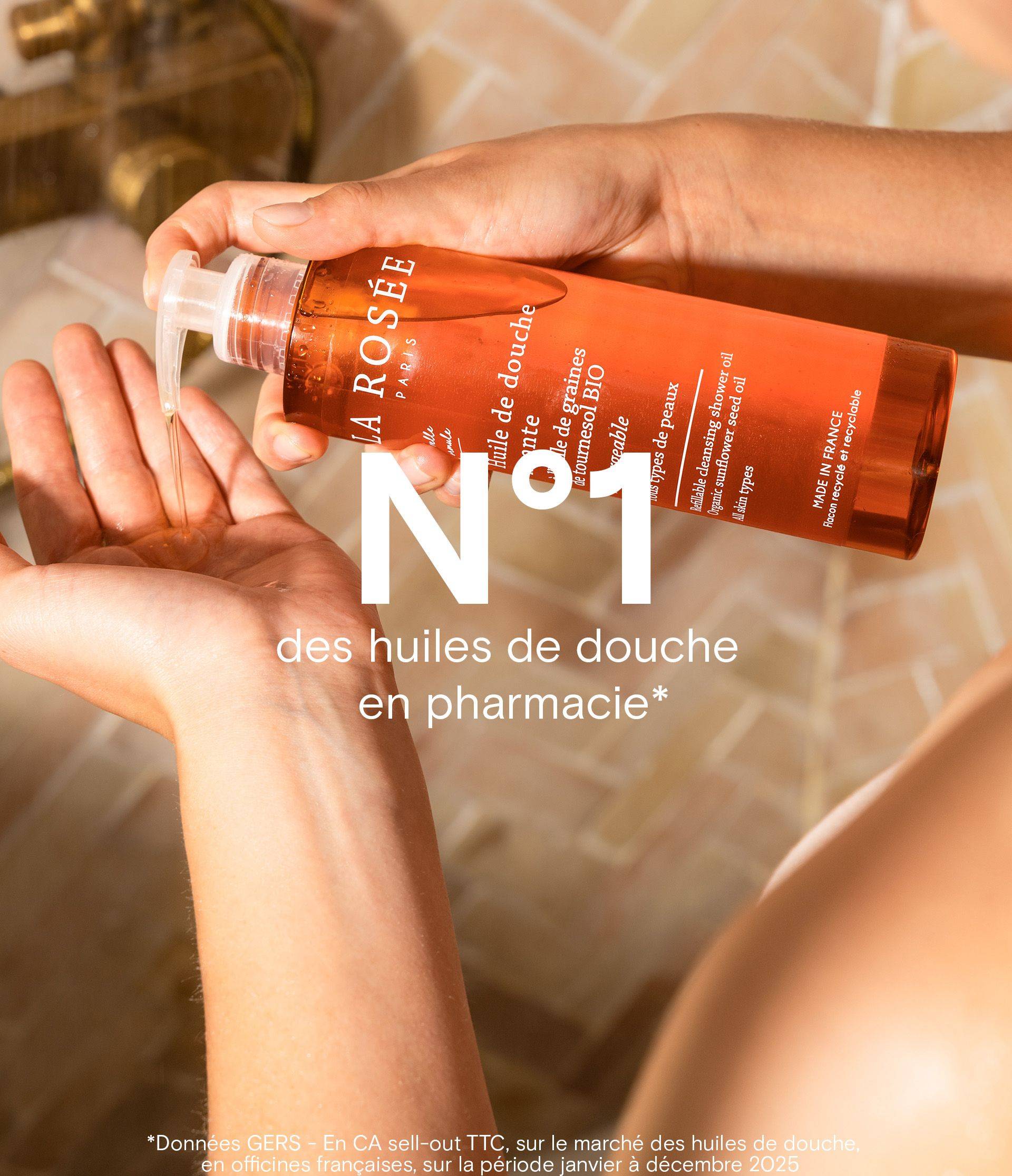 Person dispensing shower oil from an orange bottle labeled "LA ROSÉE Paris" onto their hand, with large text "N°1" overlaid.